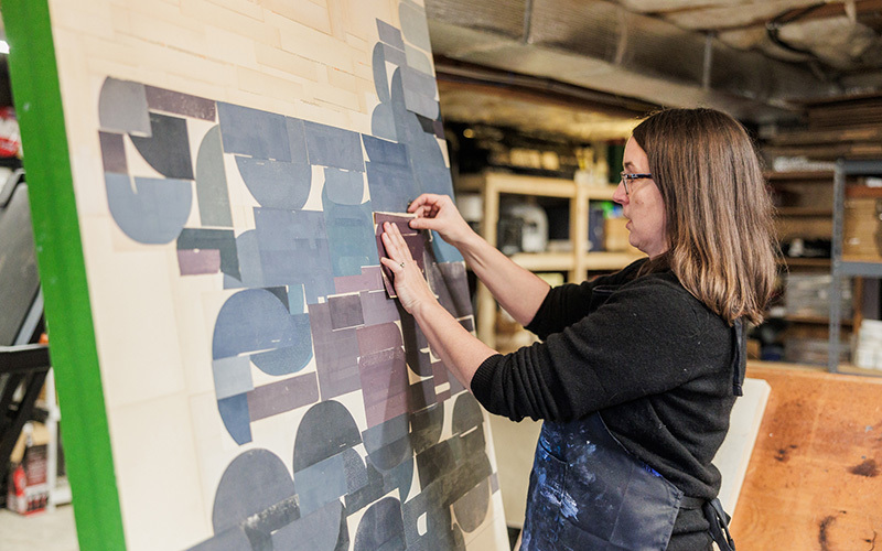 An artist standing by a large collage in her studio