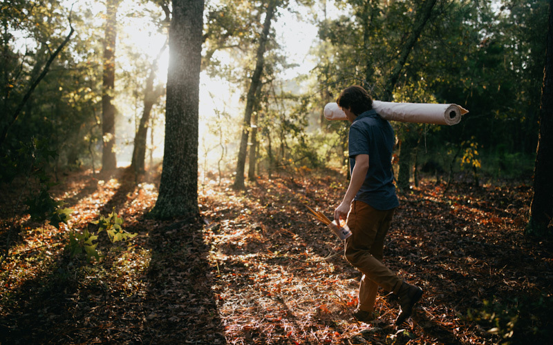 An artist carrying a canvas into the woods