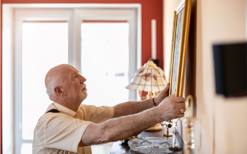 old man hangs framed artwork on a wall