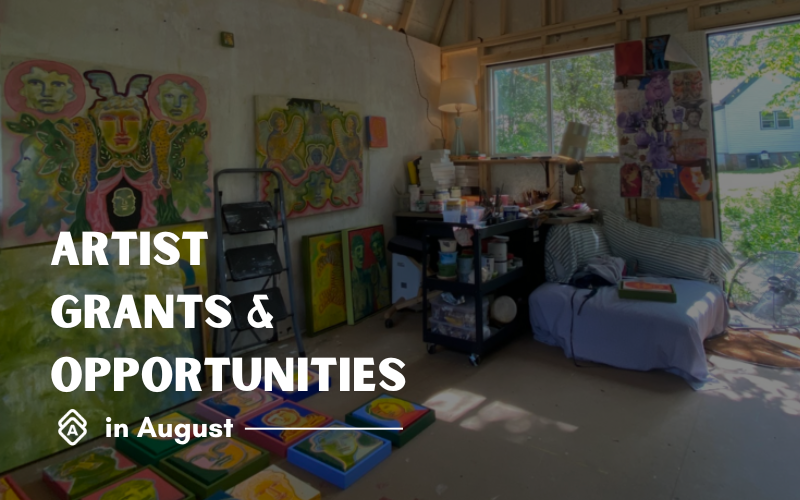 Shelby Little's bright, creative artist studio filled with vibrant artwork and artistic energy. The space features several colorful paintings displayed on easels, including works with bold yellows, greens, and reds that showcase expressive, contemporary art styles. A mobile cart holds various art supplies and materials, while a comfortable blue armchair provides a spot for reflection and planning. Large windows flood the room with natural light, creating an inspiring atmosphere for creativity. The concrete floor and white walls provide a clean backdrop that allows the colorful artwork to take center stage. This authentic studio environment represents the kind of dedicated creative workspace where artists like Shelby develop the compelling work needed for successful grant applications and career-advancing opportunities.